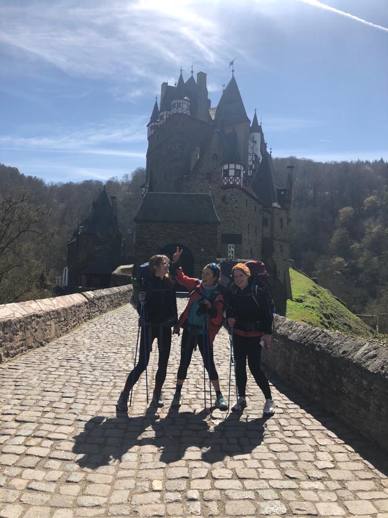 3 Wanderinnen mit Rucksack stehen vor der Burg Eltz